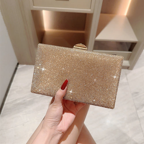 Gold glittery clutch held by a hand with red nail polish against a neutral background