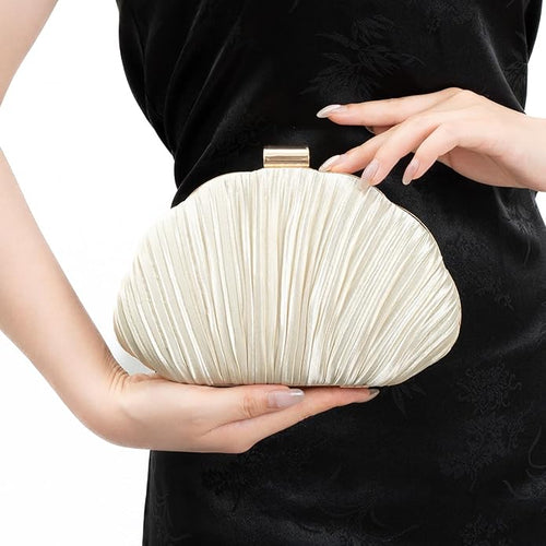 Person holding a pleated cream clutch bag against a black background