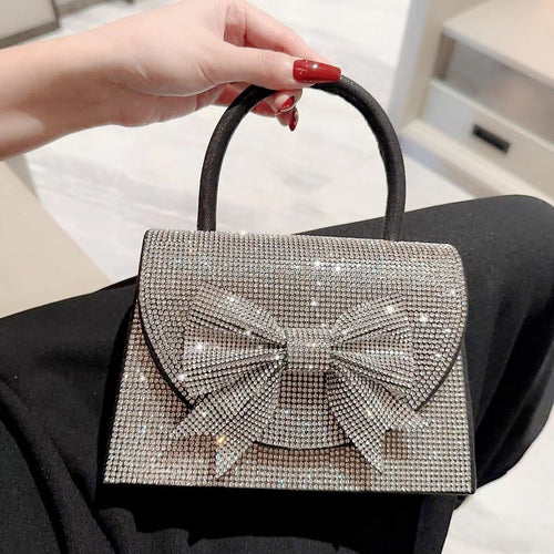 Silver handbag with a bow design held by a person with red nail polish.