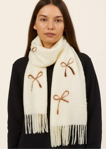 Woman wearing a cream scarf with brown bows and fringes on a beige background