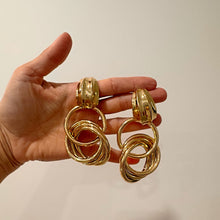 Gold hoop earrings held in a hand against a plain background