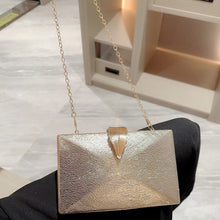 Gold clutch bag with chain strap held by a person on a marble floor.