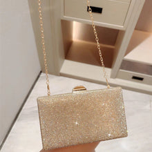 Gold glittery clutch bag with a chain strap held by a person on a light-colored floor.