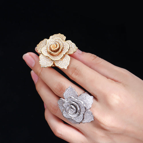 Gold and silver rose-shaped rings on a hand against a black background
