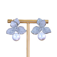 Flower-shaped earrings with pearls on a gold stand against a dark background