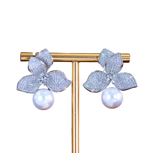 Flower-shaped earrings with pearls on a gold stand against a dark background