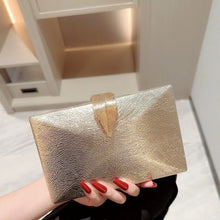 Gold clutch held by a hand with red nail polish on a neutral background