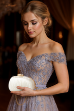Woman in an elegant off-shoulder dress holding a white clutch against a blurred background