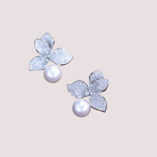 Pair of earrings with silver flower-like designs and pearls on a light pink background