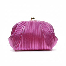 A hand holding a metallic magenta pink pleated clutch purse with a small gold clasp, set against a background of vertical gold panels with warm lighting.