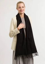 Woman wearing a black scarf with fringe, beige blazer, and gray pants on a white background