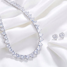 A heart-shaped crystal necklace with matching heart-shaped earrings displayed on a dark velvet surface.