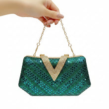 A hand holds a sparkling teal sequined clutch purse with a gold chain strap and a rhinestone-embellished V-shaped gold clasp, set against a warm beige background with vertical gold light bars.
