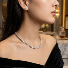 Close-up of a woman wearing a diamond necklace and earrings with a blurred urban background.